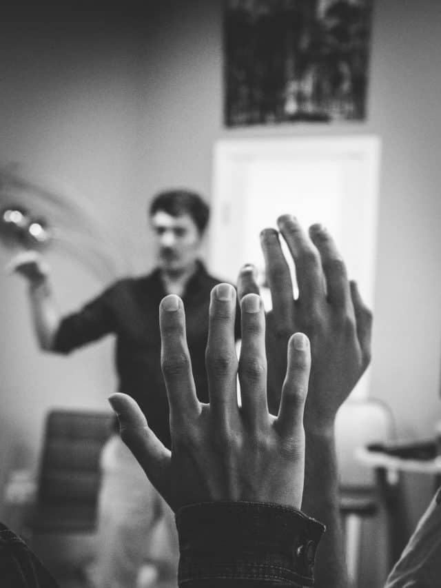 students raising hands in front of a teacher
