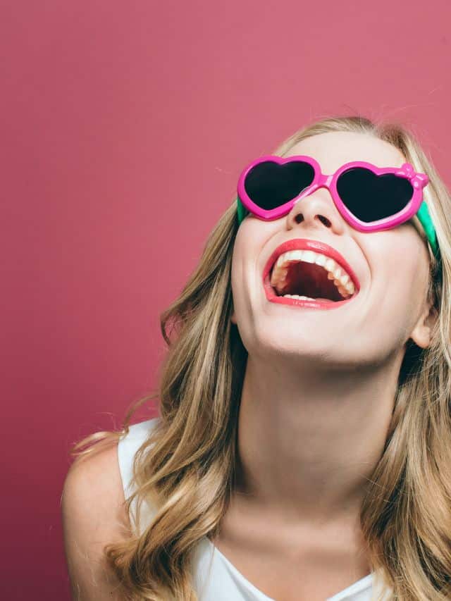 girl with sunglasses laughing in front ofpink background