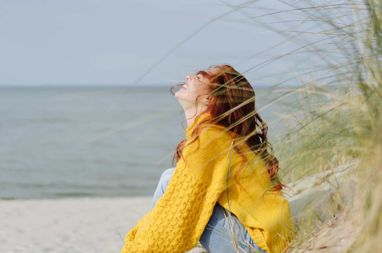 mujer feliz de amarillo sentada en la playa