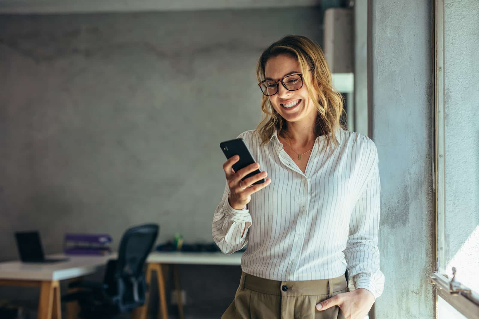 mujer feliz de pie en la oficina leyendo algo en su teléfono