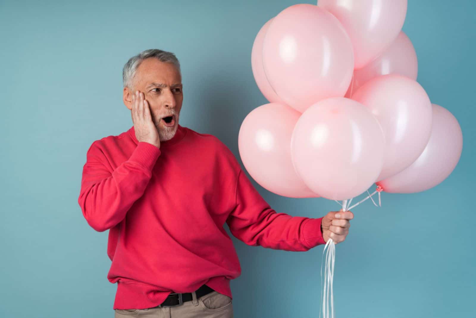 Surprised, the older man holds pink balloons in his hand