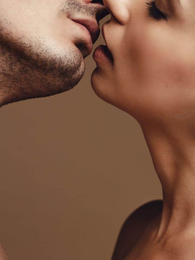 a man and a woman kissing in front of beige wall