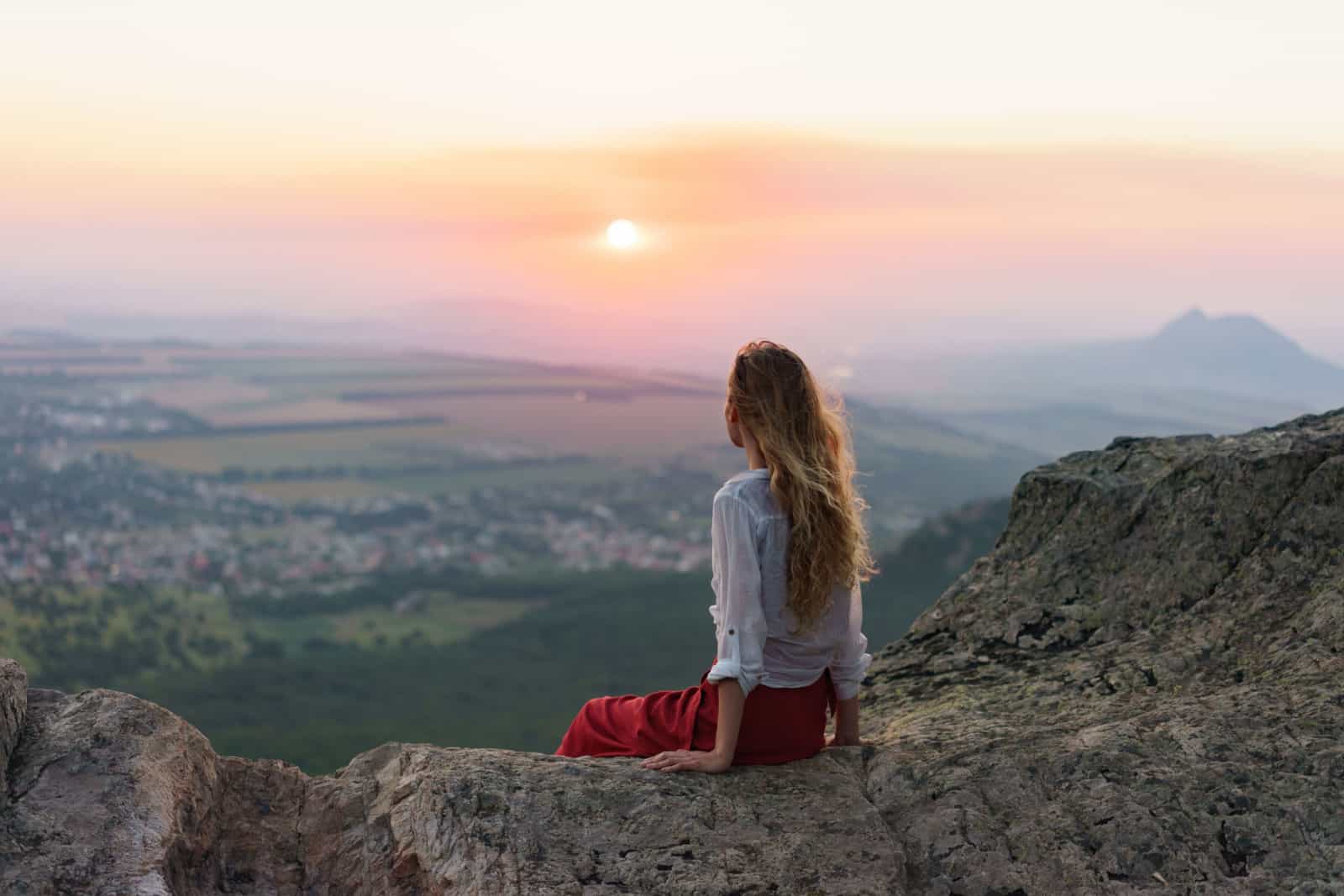 mujer en las montañas, sentada y observando la puesta de sol