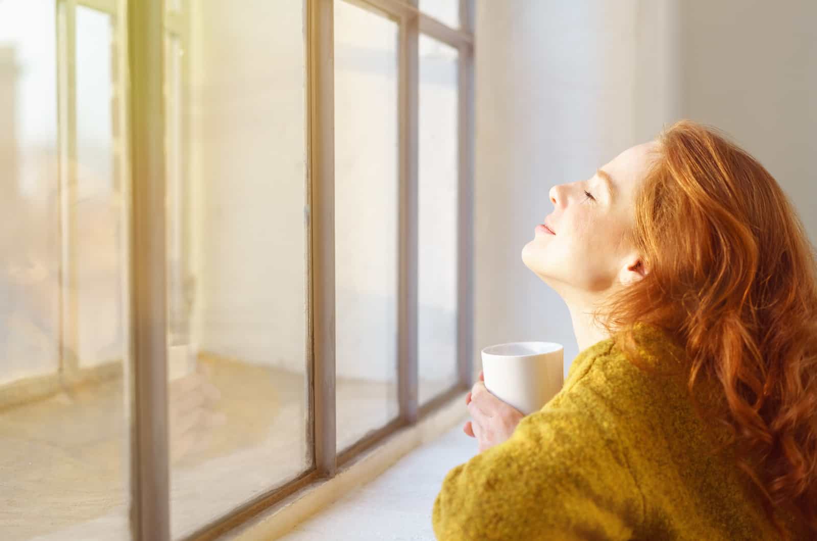 happy young woman drinking tea by window