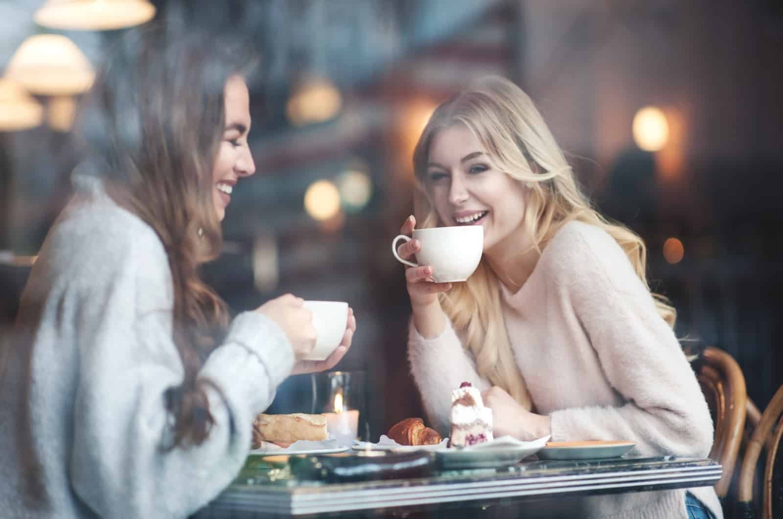 two happy friends drinking coffee in cafe shop