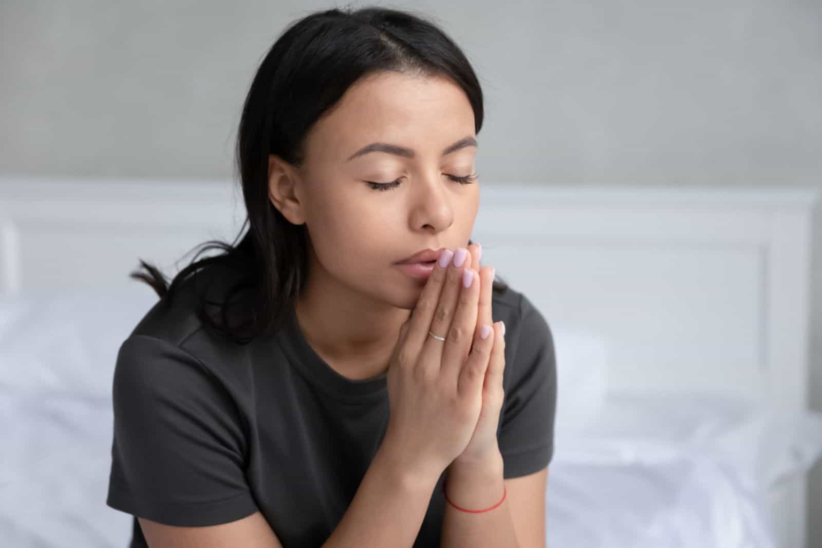 mujer joven rezando con los ojos cerrados en el dormitorio