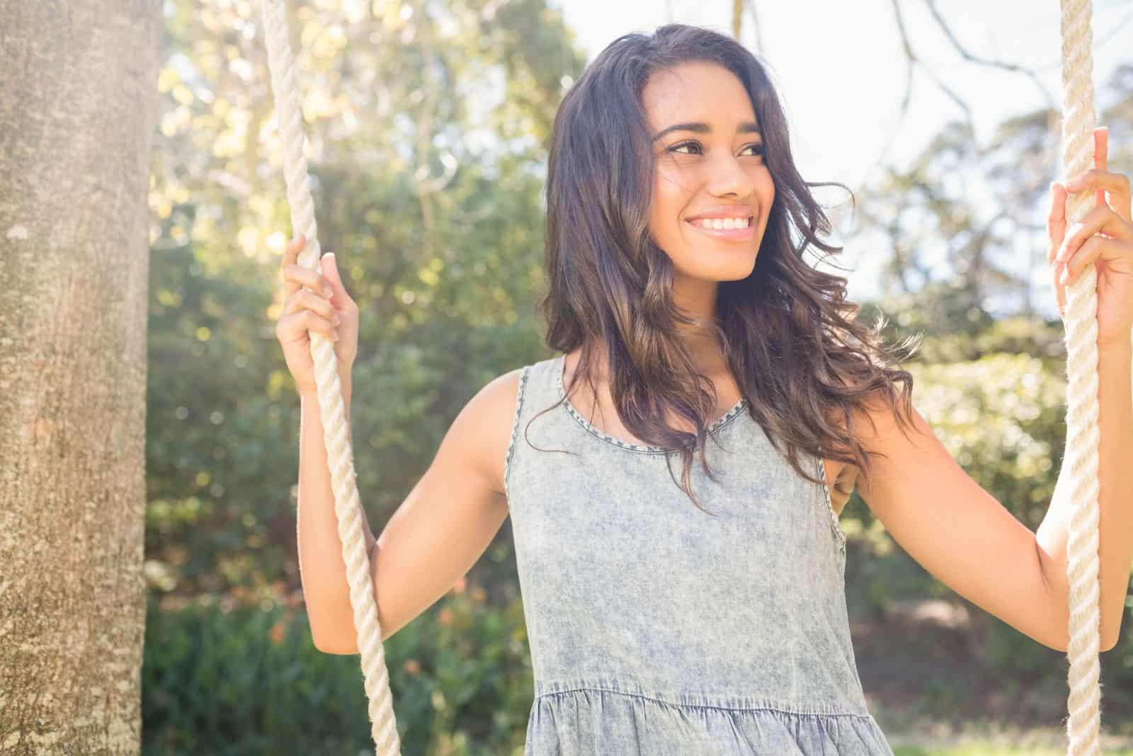 chica sonriente con pelo largo y negro en un columpio