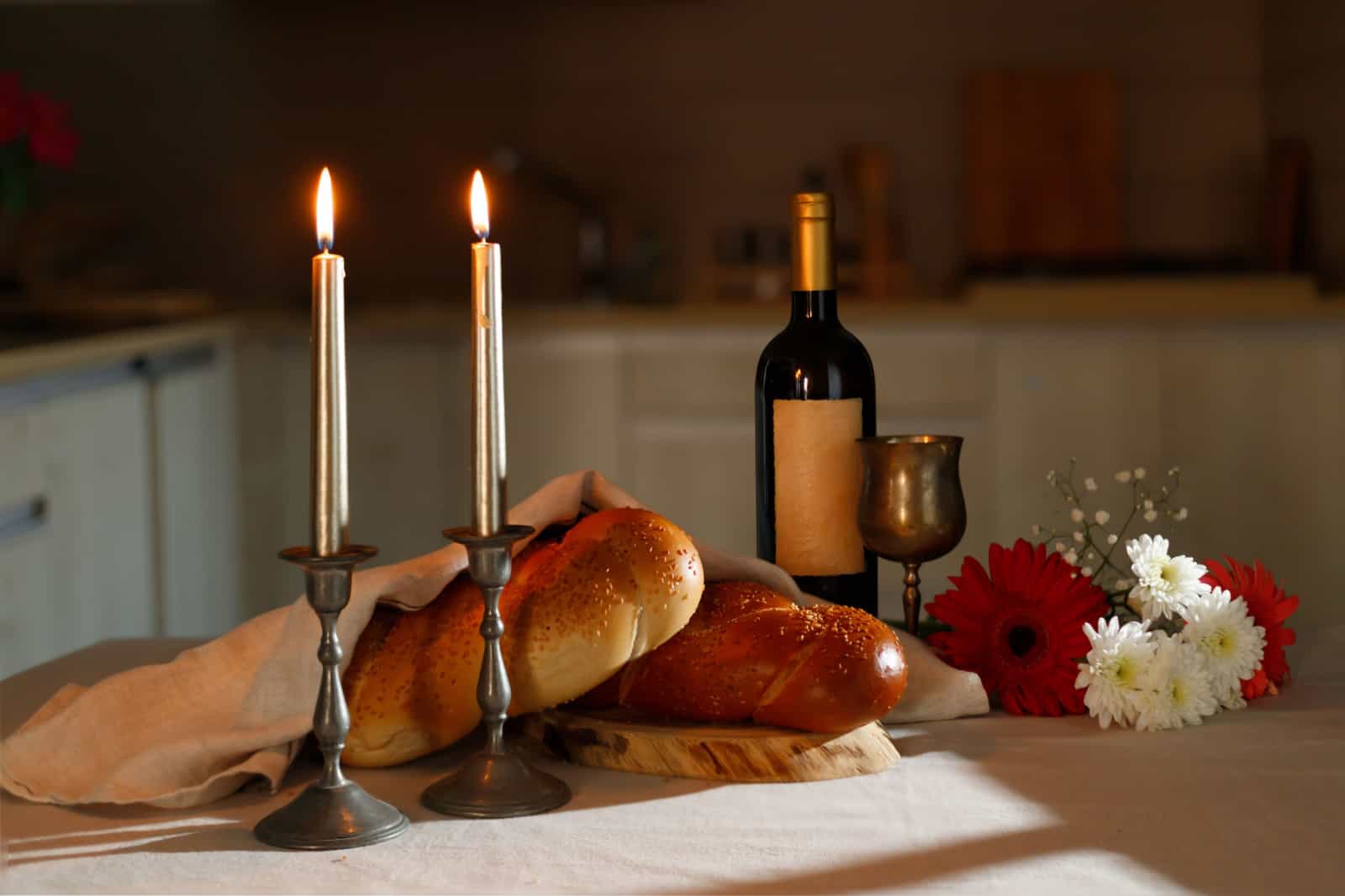 Challah bread covered with a special napkin, shabbat wine on the kitchen table. Traditional Jewish Shabbat ritual.