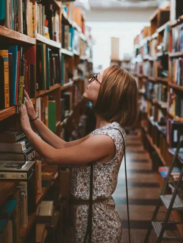 teacher in a library looking on a book shelf