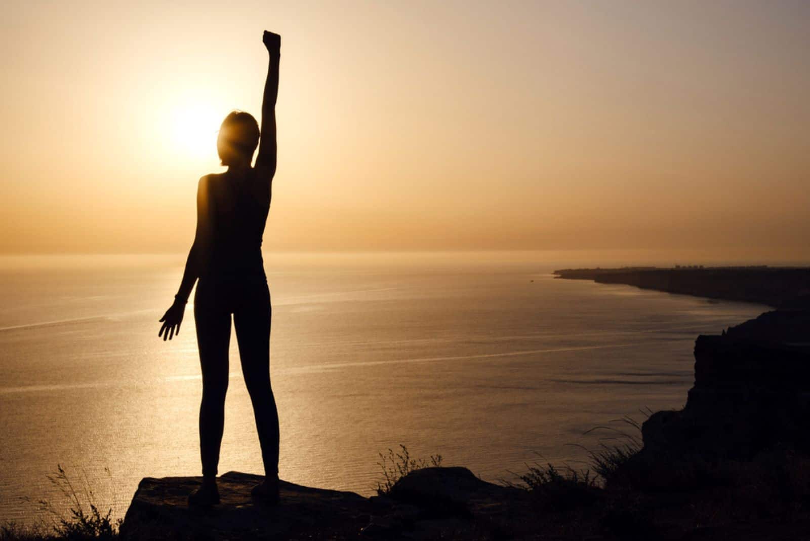Strong woman with raised hand at sunset