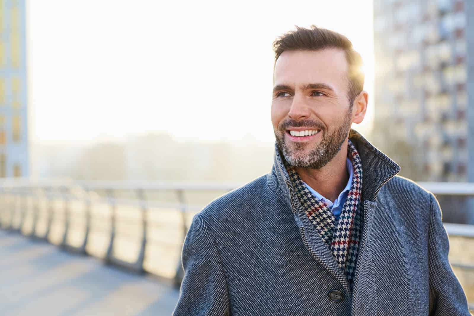 a smiling man in a coat walks down the street