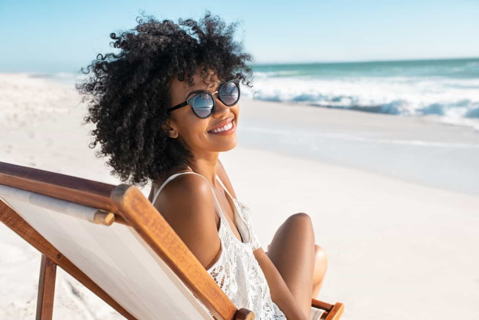 happy young black woman relaxing on wooden deck chair at tropical beach