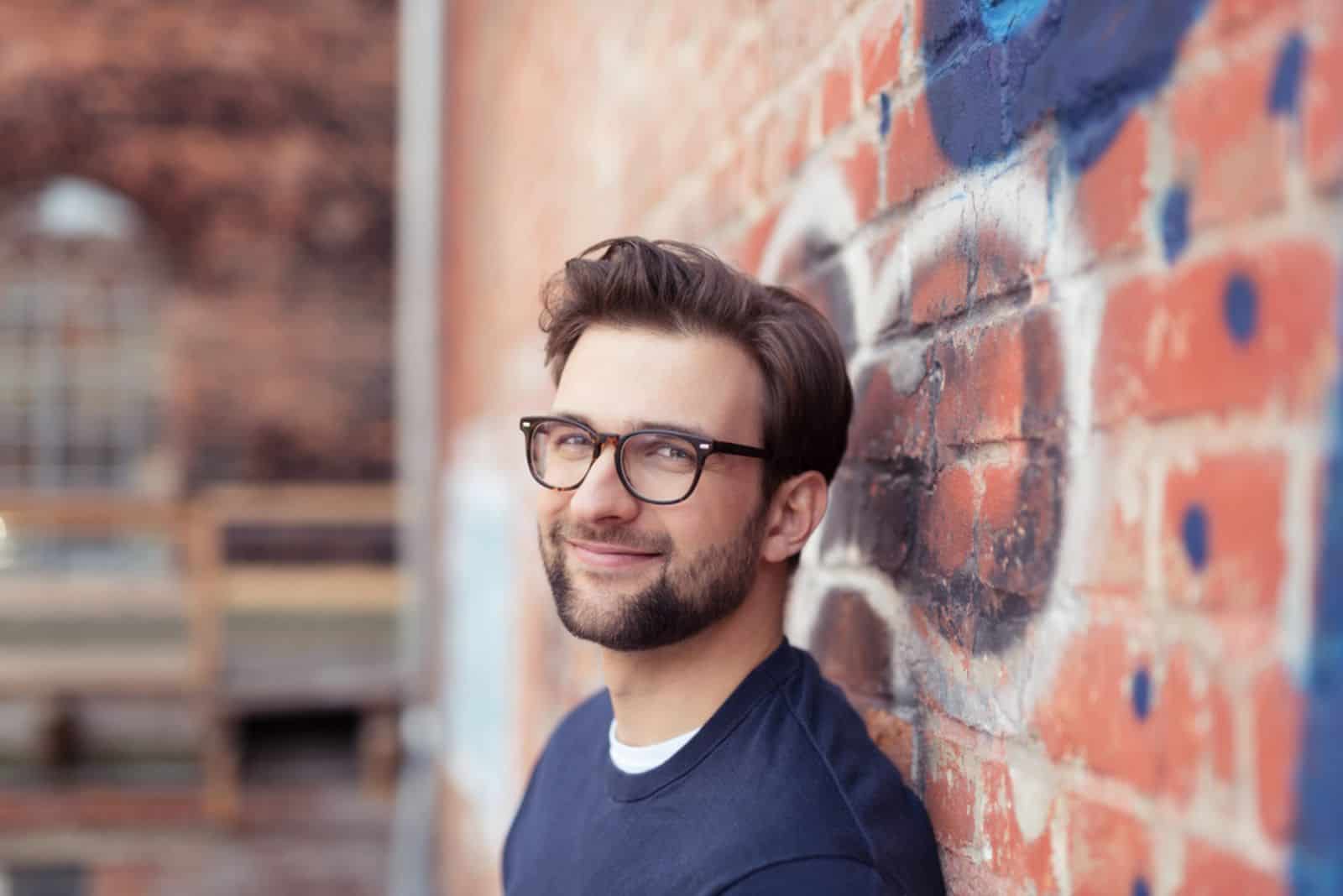 a man with glasses leaning on a brick