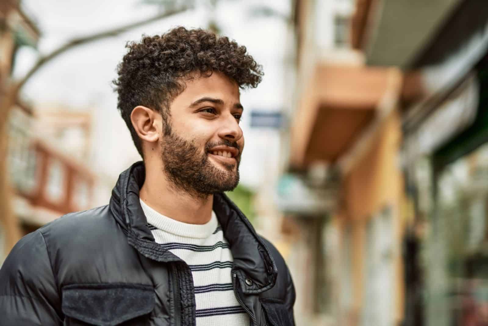 un hombre sonriente con el pelo despeinado está de pie en la calle