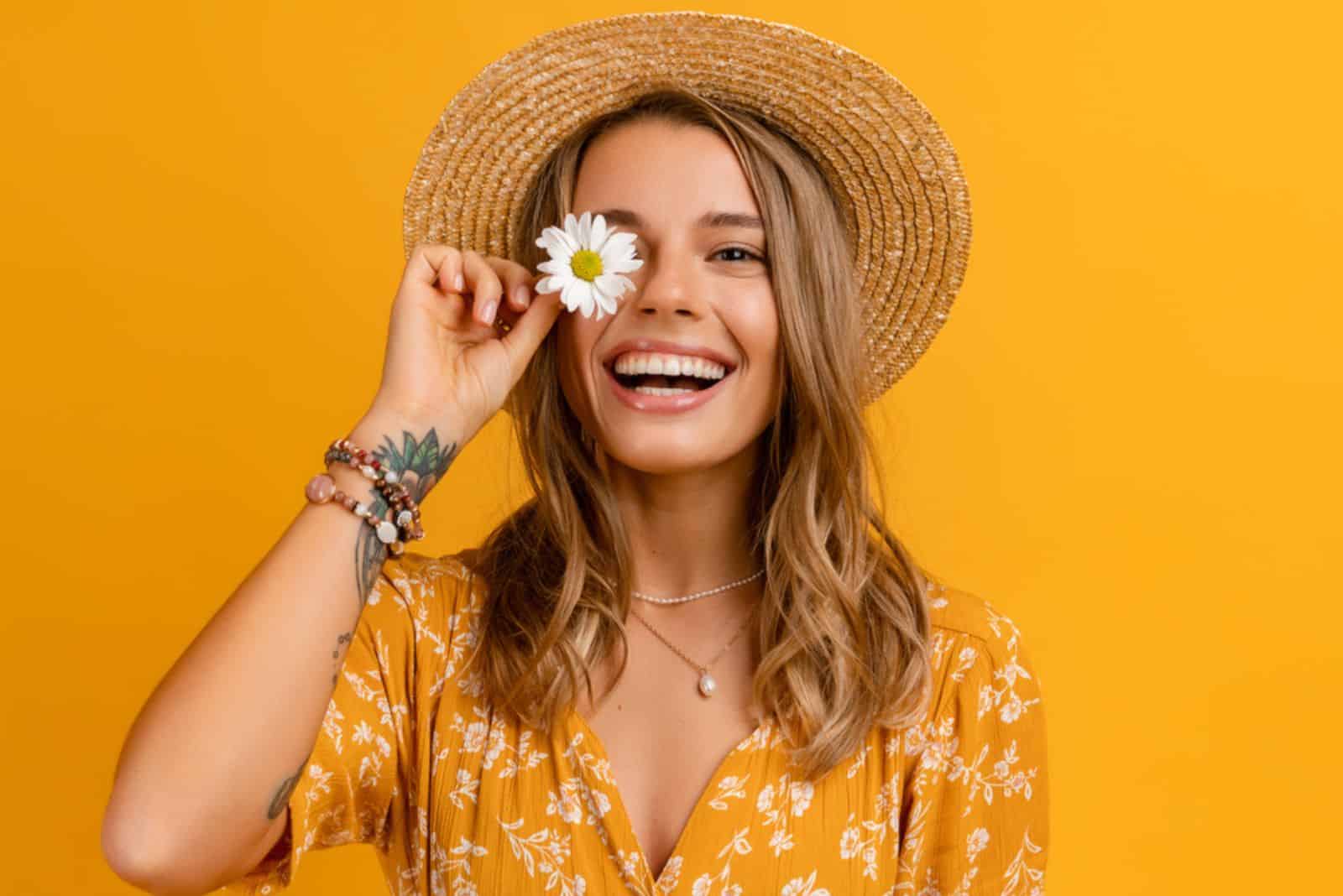  mujer con vestido amarillo y sombrero de paja sosteniendo una flor de margarita