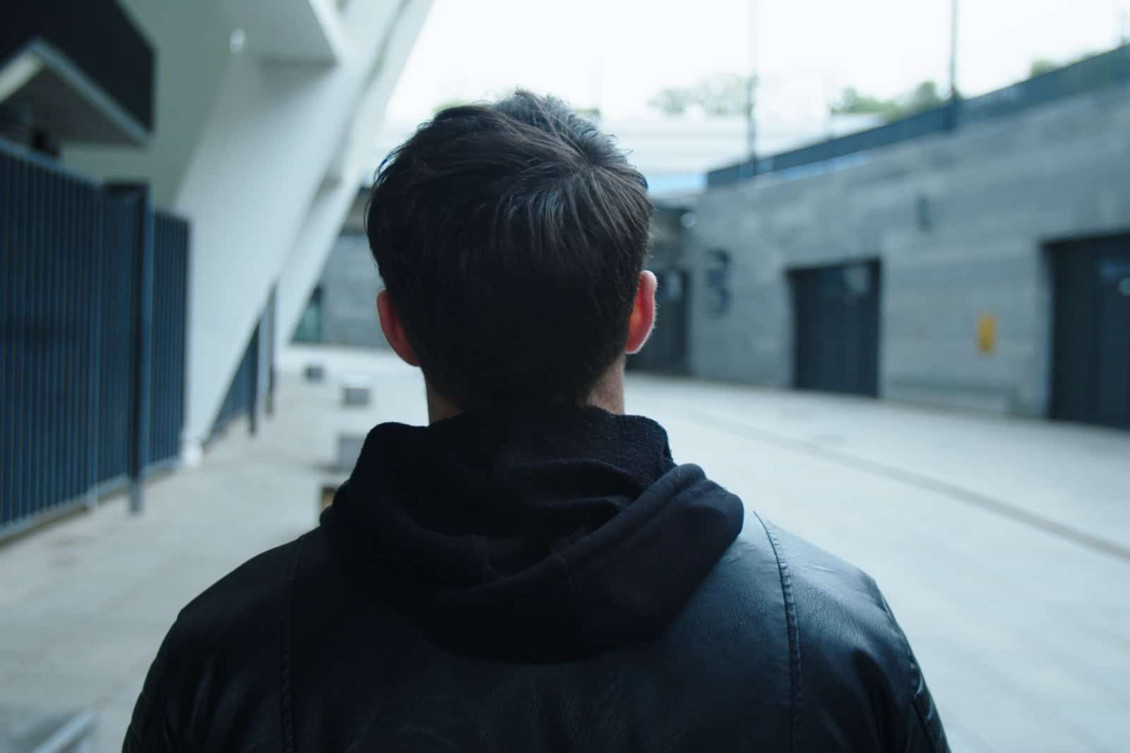 Back view of man walking on urban street in black jacket.