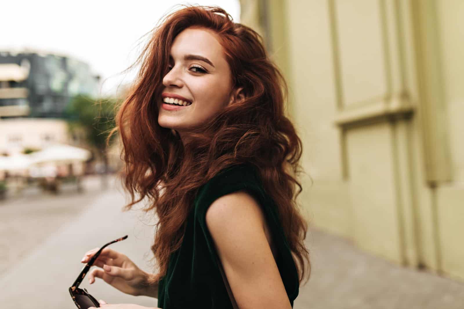 Mujer atractiva en traje verde oscuro sonriendo al aire libre