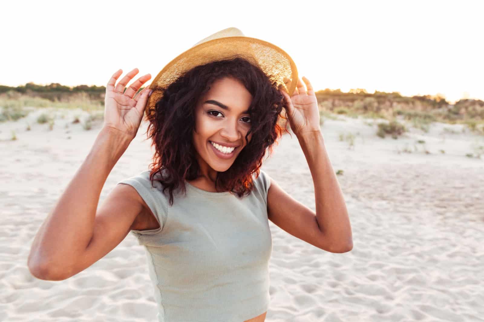 Primer plano de joven africana sonriente con sombrero de verano mirando a la cámara en la playa