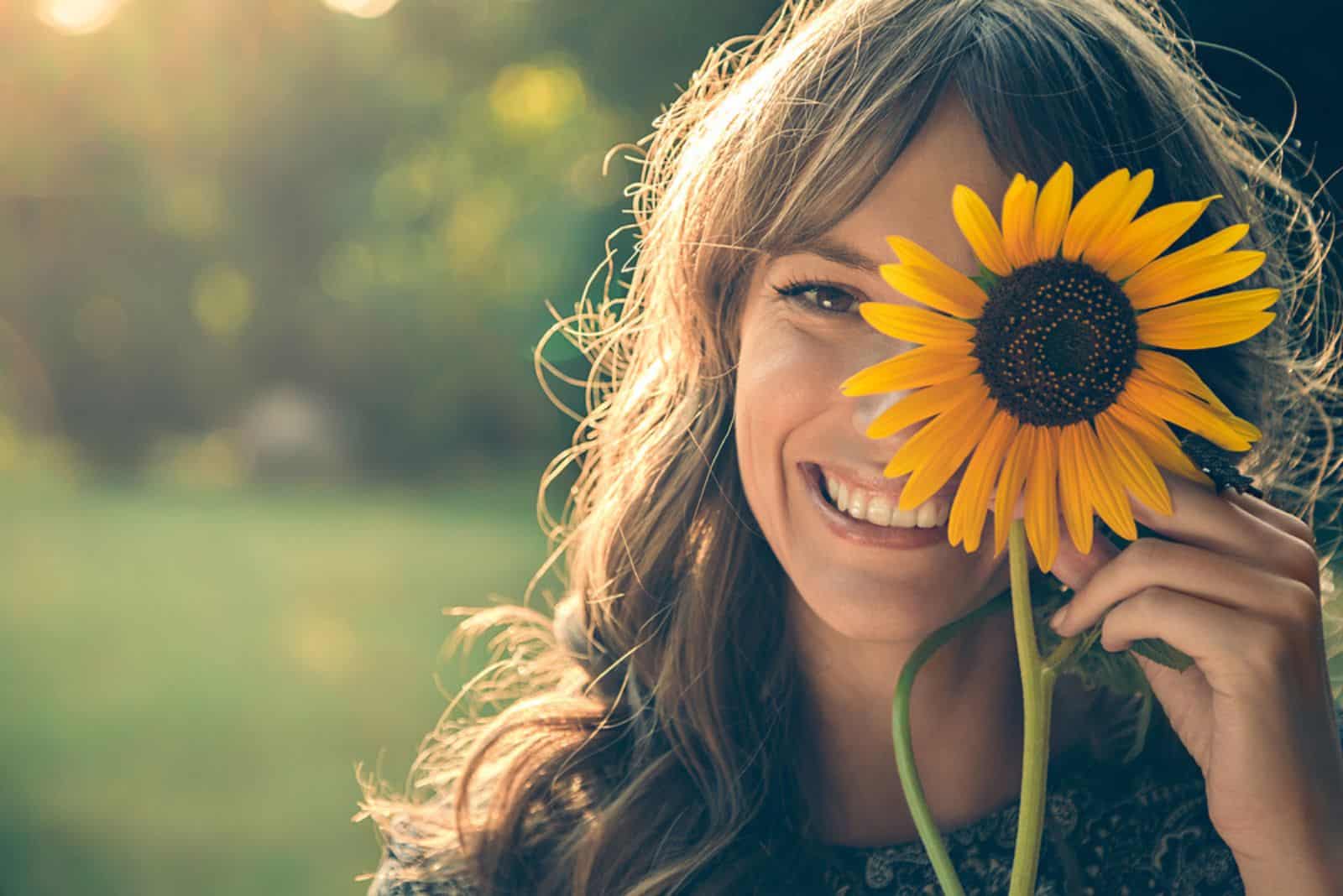 Niña en el parque sonriendo y cubriéndose la cara con un girasol