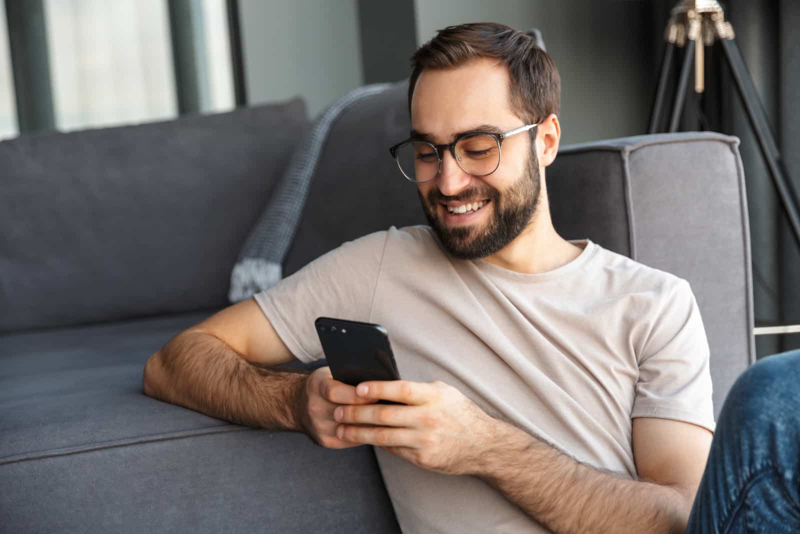 hombre sonriente sentado en el suelo y tecleando en el móvil