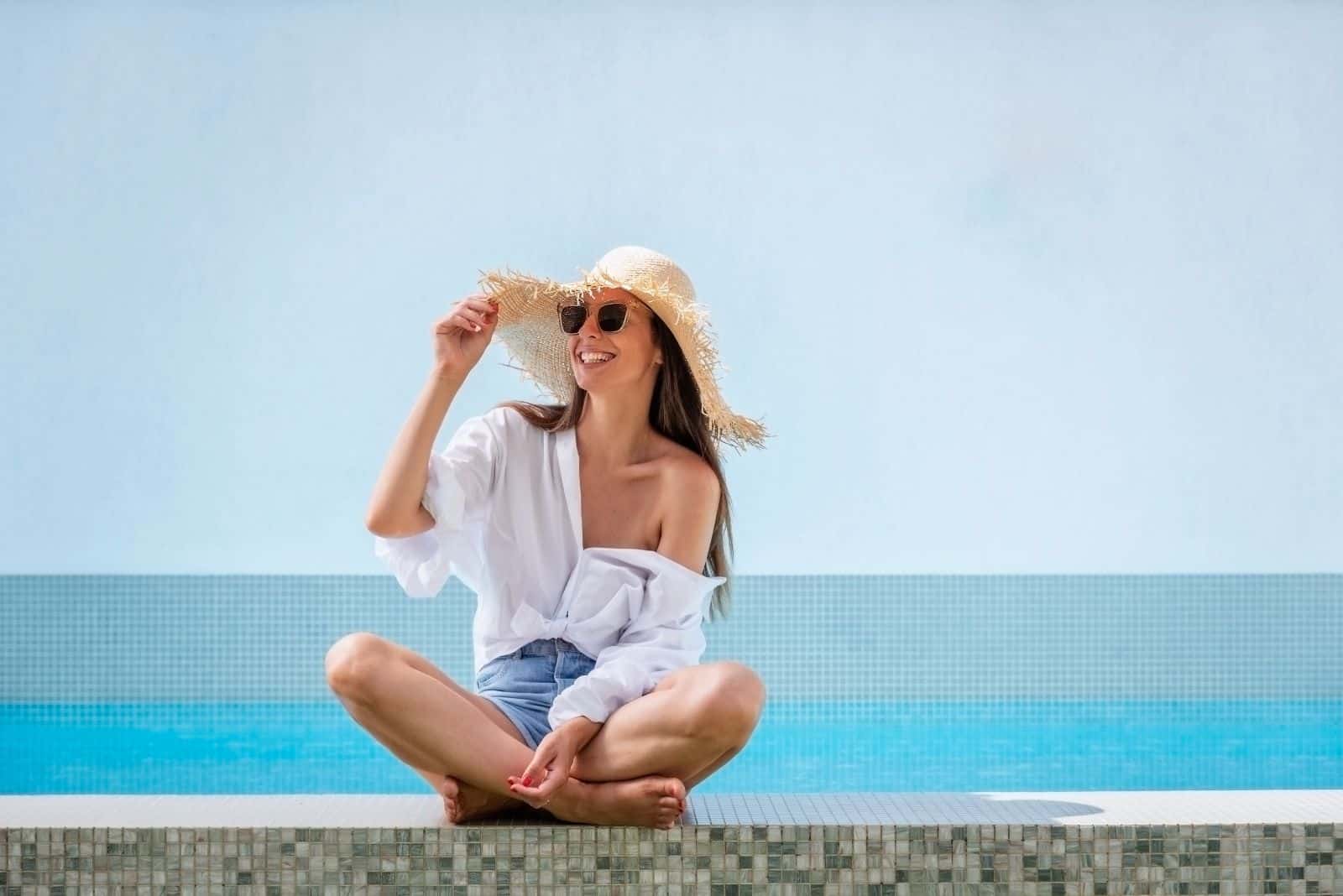 una mujer sonriente sentada en la pared con un sombrero en la cabeza