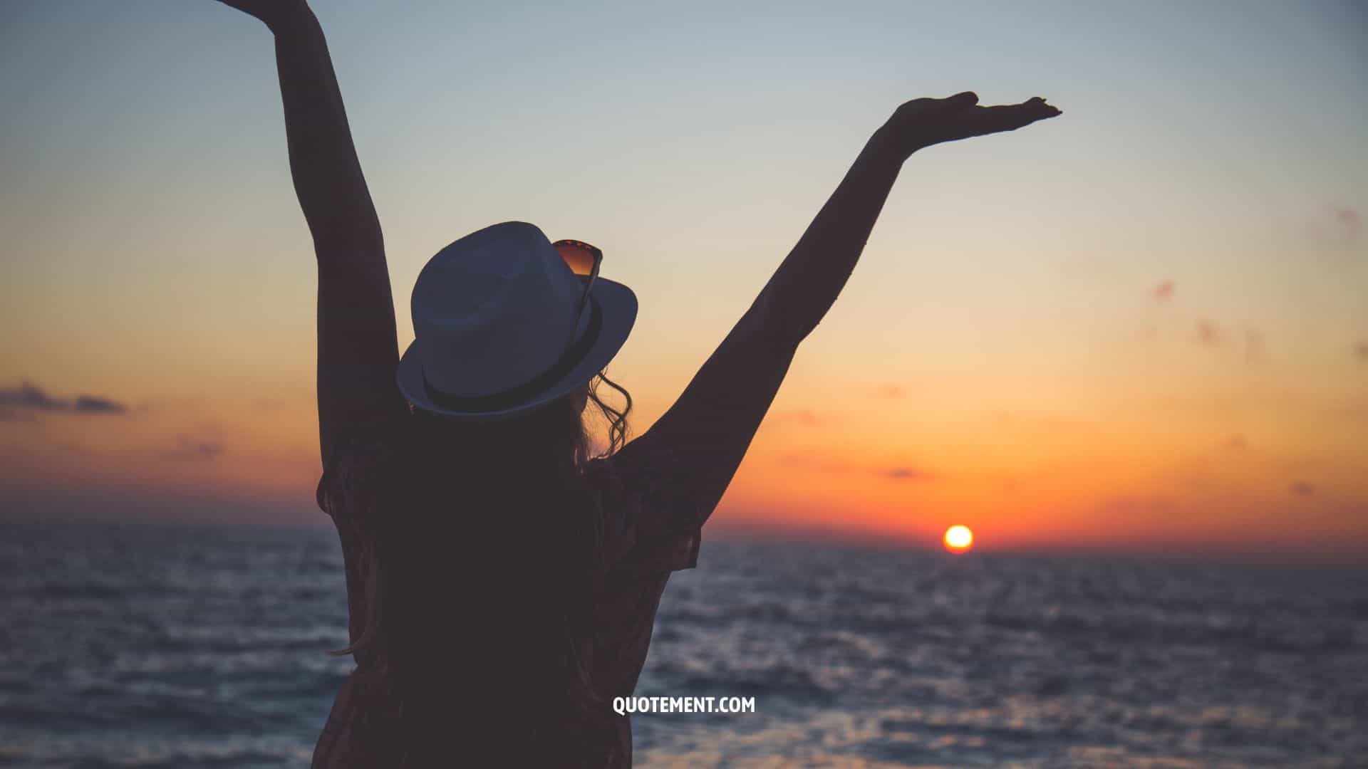 woman holding her arms up and looking at the sunset