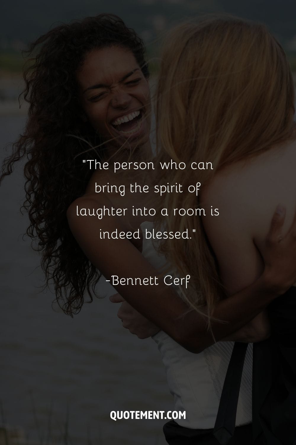 two girls hugging and laughing with the sea as backdrop