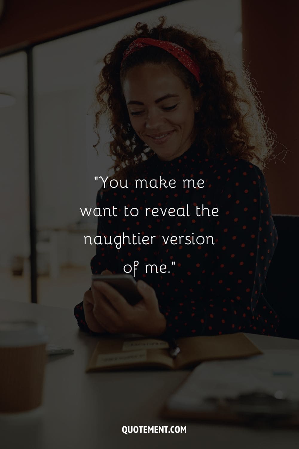 young black woman sitting at a desk, beaming as she holds her phone