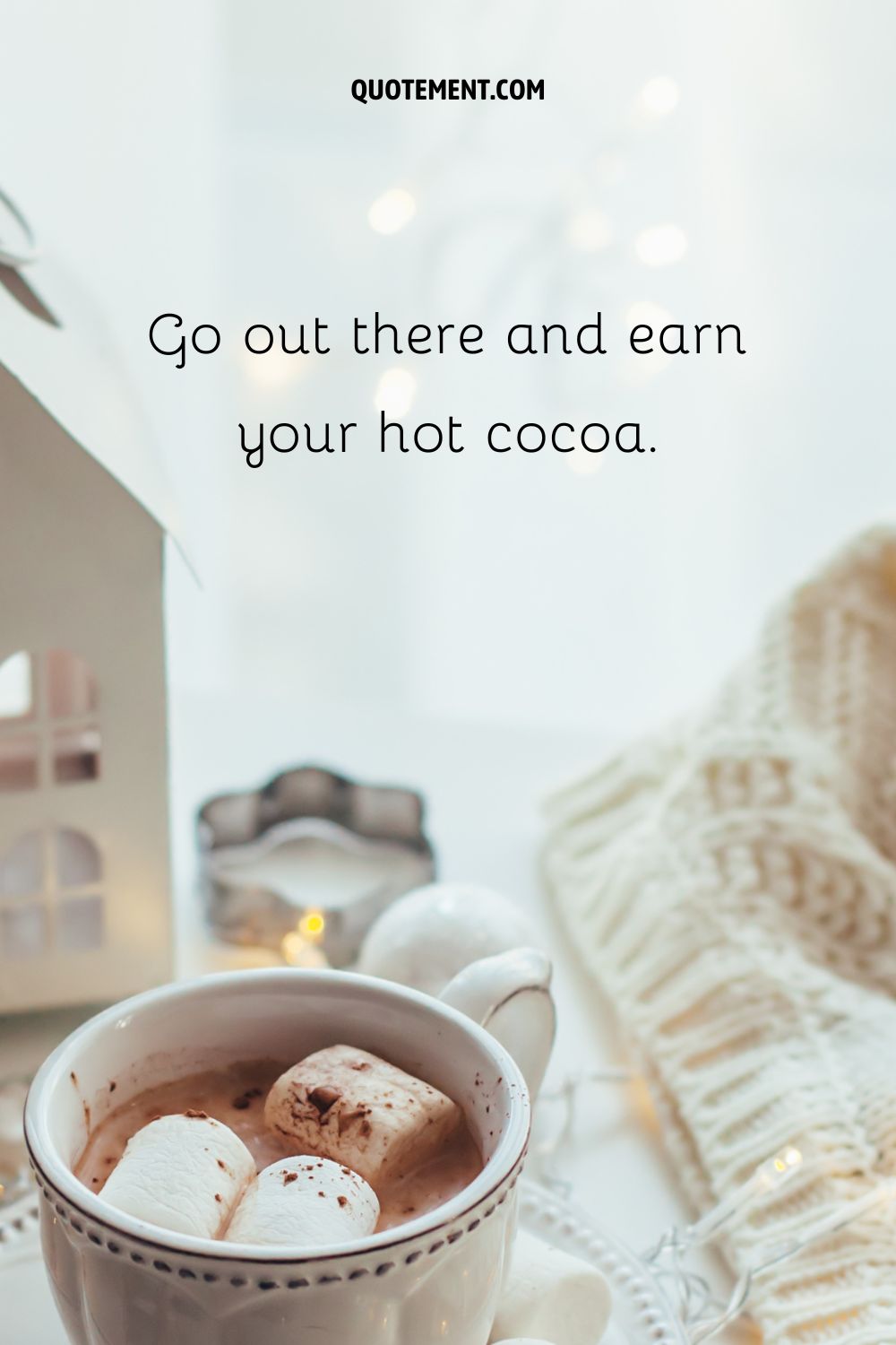 A mug of hot cocoa topped with marshmallows, a lit candle, and a knitted throw