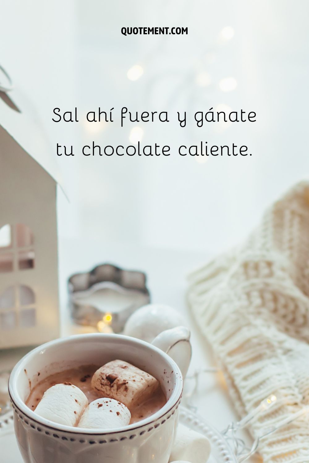 Una taza de chocolate caliente con malvaviscos, una vela encendida y una manta de punto.