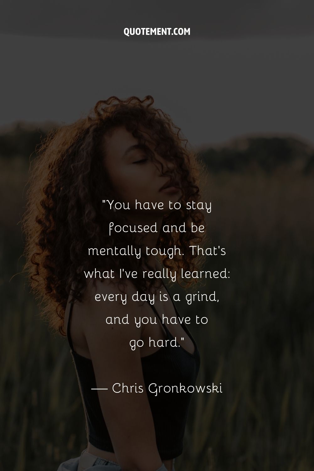 A curly-haired woman standing in a field representing an inspiring grind quote
